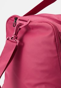 Roze tas met een gladde, gestructureerde oppervlakte. Voorzien van een rits met een zwarte trekhaak en een verstelbare riem. Compact ontwerp en stevige materialen.