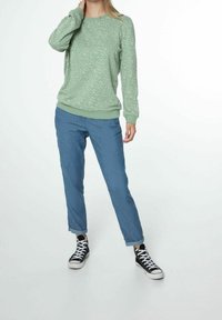 Felpa verde chiaro con macchie bianche, polsini e orlo a coste. Abbinata a pantaloni blu leggermente larghi e sneakers alte nere.