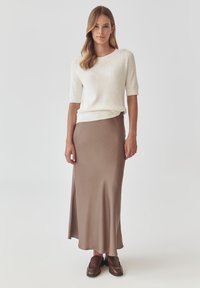 Cremefarvet kortærmet striktop med ribbede manchetter, parret med en lang taupe silkeskjørt. Modellen har brune lædersko på. Minimalistisk design.