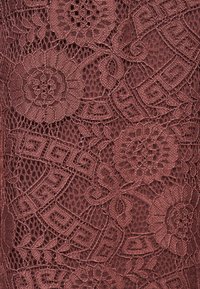 Αναλυτικό κοντινό πλάνο ύφασματος δαντέλας σε κοκκινωπό-καφέ απόχρωση με λουλουδένια και γεωμετρικά σχέδια και περίπλοκες υφασμένες υφές.