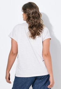 Helles graues T-Shirt mit dezentem Streifenmuster und kurzen Ärmeln, kombiniert mit dunklen Jeans, von hinten betrachtet.