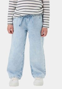 Pantalones de mezclilla de color azul claro con un corte holgado, cinturilla elástica y cordón. Se combinan con una blusa blanca con rayas marino y zapatillas blancas.
