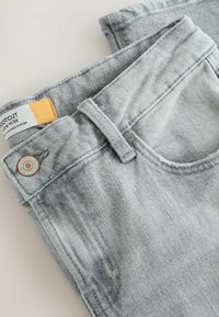 Lichtgrijze denim jeans met een lage tailleband, voorzien van een gele label, zilveren knoopdetails en een licht vervaagde textuur.