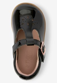 Schwarze Lackleder-Mary-Jane-Schuhe mit ausgeschnittenem Blumenmuster, einem Schnallenriemen und einer hellbraunen Sohle. Innenfutter in Hellrosa.