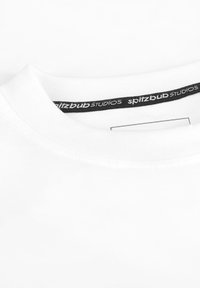 Witte katoenen T-shirt met een ronde halslijn, geribbelde kraag en een zwart label met "spitzbub STUDIOS" in witte tekst.