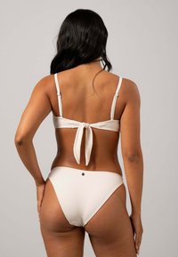 Vitt bikini-set med knytbak, smala axelremmar, mjuk textur och en liten dekorativ detalj på baksidan av trosorna.