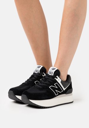 Black suede and mesh sneakers with a white accent, featuring a thick black rubber sole and a prominent 'N' logo on the side.