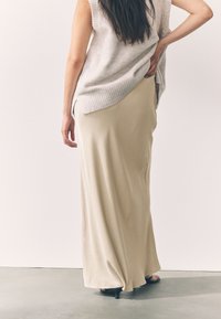 Beige, flödande maxikjol i lätt tyg, kombinerad med en ljusgrå, ärmlös stickad topp. Outfitten har en avslappnad passform.