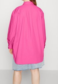 Langsleeve, oversized shirt in felroze katoen met een achterlijke yoke en zijslitsen, gecombineerd met een lichte denim rok.