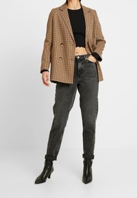 Brauner und schwarzer kariert Doppelreiher-Blazer über einem schwarzen Cropped-Top, kombiniert mit high-waisted schwarzen Jeans und schwarzen Stiefeletten.