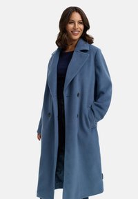 Blå fleece-kappa med slagkrage, dubbelknäppt knappslå, sidofickor och en texturerad yta. Rak silhuett.