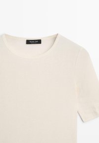 Pull à manches courtes de couleur crème avec un col rond, étiquette noire Massimo Dutti cousue à l'intérieur du col.