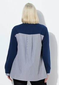 Marinblå och vit randig långärmad topp med en enfärgad marinblå övre del och veck i ryggen; har en rund halsringning och knäppta ärmslut.