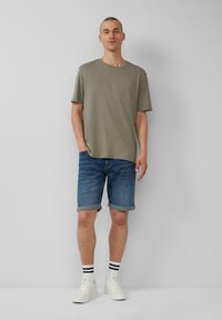 T-shirt olive vert à manches courtes, shorts en denim avec ourlets, baskets blanches et chaussettes à rayures noires. Design simple avec une coupe décontractée.