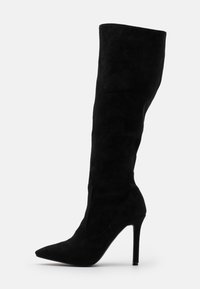 Bota de tacón de aguja de ante negro hasta la rodilla con punta puntiaguda y textura suave. Cuenta con un caña ajustada y un detalle mínimo de costura lateral.