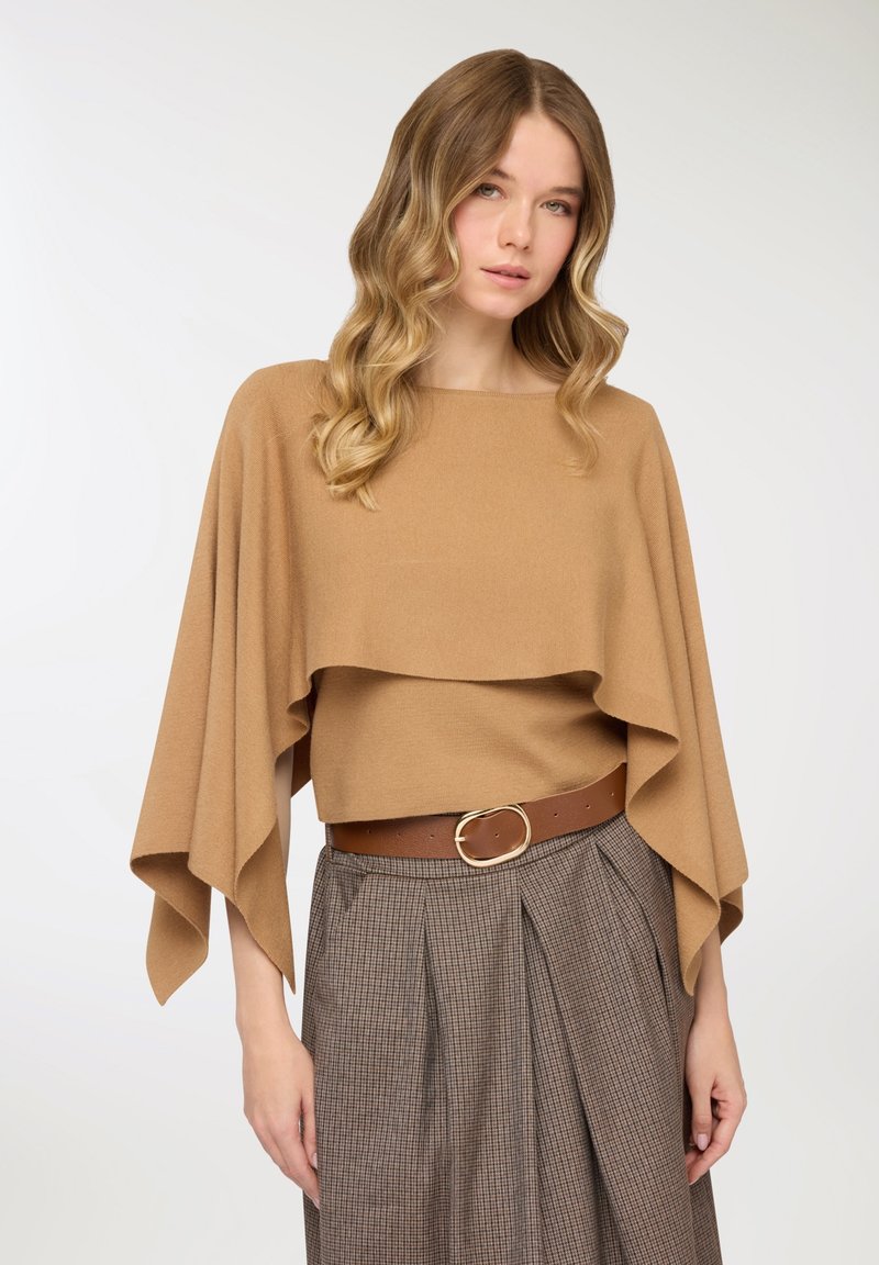 Top a strati color tan realizzato con materiale morbido, caratterizzato da un collo a barchetta e maniche ampie, abbinato a una cintura marrone su una gonna a quadri.