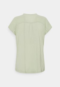 Blusa verde chiaro a maniche corte con scollatura tonda, tessuto morbido e discreti dettagli di pieghe sul retro. Tessuto liscio con vestibilità comoda.