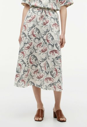 Falda midi con estampado de leopardo en rojo y negro, cintura con cordón, combinada con top a juego y sandalias marrones de tacón ancho y punta abierta.