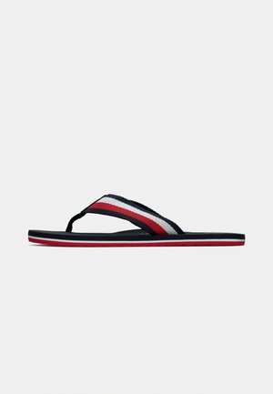Flip-flop sandaalit, joissa on punaiset, valkoiset ja tummansiniset raitakankaiset hihnat ja vastaava raitapohja, esitetty sivulta yksinkertaisen taustan päällä.
