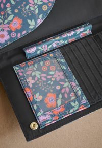 Peněženka s květinovým vzorem v námořnické modré a černé barvě. Obsahuje průhlednou kapsu na ID a několik slotů na karty. Disponuje zlatým zapínáním na druk.