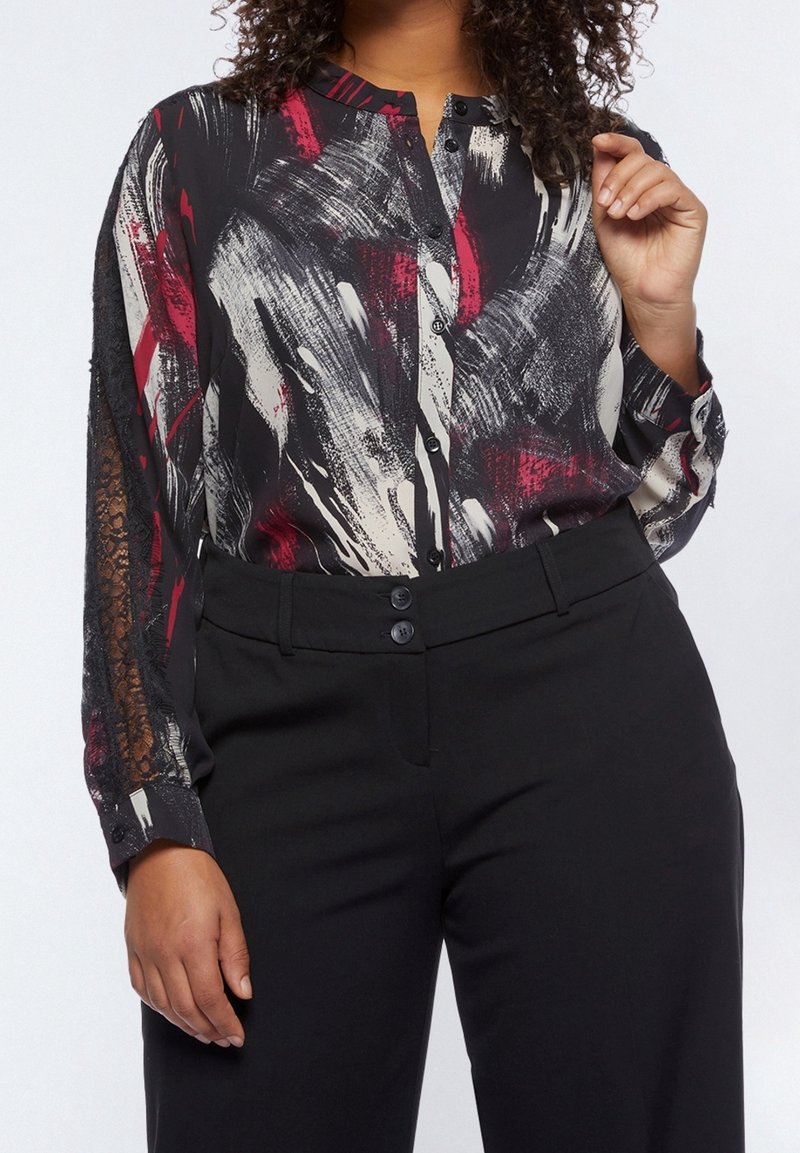 Blusa a maniche lunghe nera con un motivo astratto colorato. Presenta una chiusura con bottoni e dettagli in pizzo trasparente sulle maniche.