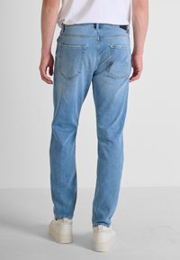 Jeans de mezclilla azul claro con un corte ligeramente ajustado, que cuentan con dos bolsillos traseros, costuras sutiles y se combinan con zapatillas blancas.