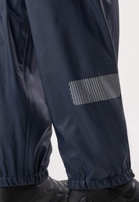 Navy waterproof pants with elastic cuffs and a reflective striped patch on the lower leg, paired with black outdoor shoes.