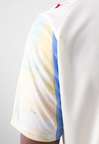 Majica kratkih rukava za sport s bijelim, teksturiranim tijelom; višebojni tie-dye uzorak u mekanim nijansama žute, plave i ružičaste na rukavima.
