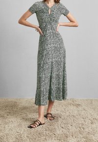 Black and white striped midi dress with short sleeves, featuring a keyhole detail at the neckline and a flowing silhouette. Worn with strappy black sandals.