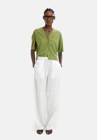 Zielona krótka koszula z guzikami i krótkim rękawem, z złotym akcentem; w komplecie z luźnymi białymi spodniami. Czarne sandały na odsłonięte palce.