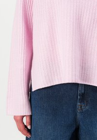 Pulover roz deschis, cu textură în dungi, cu croială lejeră și mâneci largi, asortat cu blugi din denim albastru închis, cu croială dreaptă și cusături vizibile.