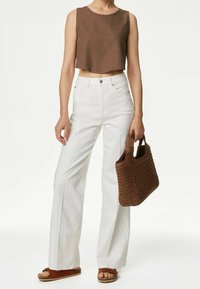 Jeans de pierna ancha blancos combinados con un top corto de lino marrón; bolso trenzado marrón; modelo con sandalias marrones.