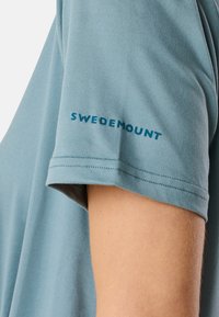 Kortärmad t-shirt i ljusblått, tillverkad av mjukt tyg. Har en teal-färgad logotyp "SWEDEMOUNT" längs ärmen för varumärkesprofilering.