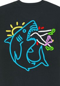 T-shirt noir avec un design de requin brodé en bleu, rehaussé d'accents colorés incluant du rouge, du vert, du jaune et une fleur rose.