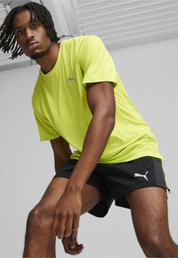 Camiseta deportiva verde lima con mangas cortas y logotipo reflectante, combinada con pantalones cortos negros que tienen detalles laterales y logotipo.