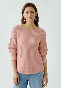 Helle rosa gerippte Pullover mit langen Ärmeln und einem weiten Ausschnitt, aus strukturiertem Strickmaterial, kombiniert mit hellblauen Jeans.