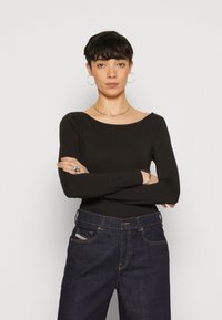 Schwarzes Langarmoberteil mit weitem Ausschnitt, kombiniert mit dunkelblauen Jeans aus Denim mit klassischem Design und sichtbaren Nähten.