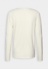 Bluzka z długim rękawem w kolorze ecru, wykonana z teksturowanej tkaniny, z okrągłym dekoltem i luźnym krojem oraz prostym wykończeniem na dole.