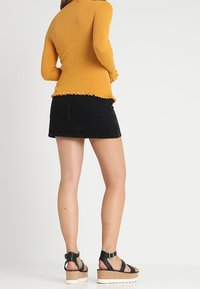 Keltainen ribbattu pitkähihainen paita, jossa on purjeompelukset, yhdistettynä mustaan denimp mini-hamoon ja mustiin korsettikorkokenkiin, joissa on korkkipohjat.