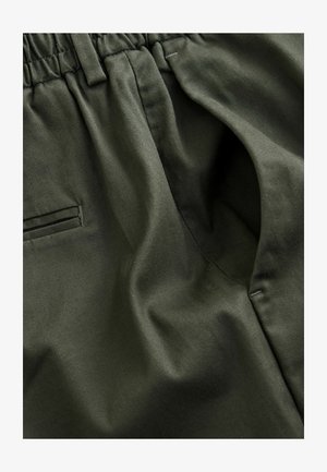 Tissu vert olive avec une texture douce ; présente une taille élastique et des poches latérales ; détails de coutures lisses visibles.