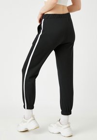 Pantalones de chándal negros con una raya blanca en los lados, cinturilla elástica y puños, fabricados con un material suave, ideales para un look casual.