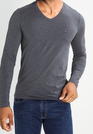 Szara, długorękawowa koszulka w serek, wykonana z miękkiego materiału, z małym logo na piersi i dopasowanym krojem, zestawiona z niebieskimi dżinsami.