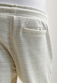 Ljust grå sweatpants med en mjuk, texturerad yta. Har en liten bakficka och elastisk midja med rynkad detalj.
