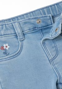 Hellblaue Jeans aus Denim mit figurnaher Passform. Zu den Merkmalen gehören eine florale Stickerei auf der Tasche, ein Metallknopfverschluss und kontrastierende Nähte.
