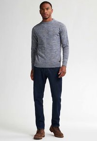 Szary i niebieski sweter z melanżowego dzianiny z okrągłym dekoltem, ściągaczami na mankietach i dole. Połączony z ciemnoniebieskimi dżinsami i brązowymi butami na sznurowadła.