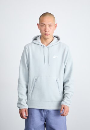 Jasnoniebieska polarowa bluza z kapturem z kangurzą kieszenią z przodu, zamkami błyskawicznymi po bokach i małym białym logo Nike na piersi. Miękka tekstura i casualowy design.