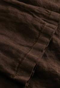Gros plan sur un tissu brun foncé avec des coutures visibles et de subtils plis.