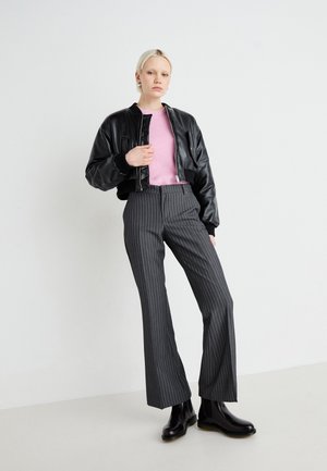 Black leather bomber jacket over a pink sweater, paired with grey pinstriped wide-leg trousers and black ankle boots. Smooth textures and fitted design.