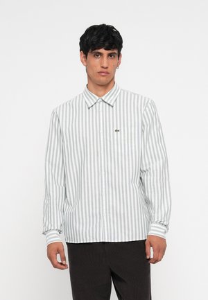 Button-up shirt featuring light gray and white vertical stripes, long sleeves, and a small embroidered logo on the chest pocket.