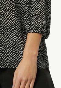Schwarz-weiße Bluse mit Zebramuster und kurzen, elastischen Ärmeln. Leichter, strukturierter Stoff mit lockerer Passform. Der Saum ist leicht gewölbt.